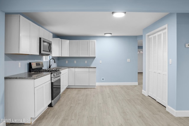 kitchen with stainless steel appliances, baseboards, white cabinets, light wood-type flooring, and dark stone countertops