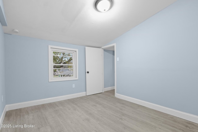 spare room with vaulted ceiling, light wood-style floors, and baseboards