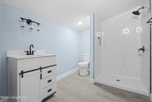 bathroom with a marble finish shower, toilet, vanity, wood finished floors, and baseboards