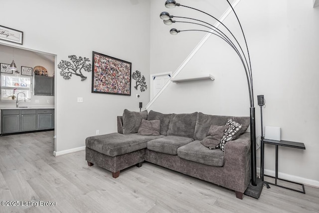 living room with a high ceiling, baseboards, and light wood finished floors