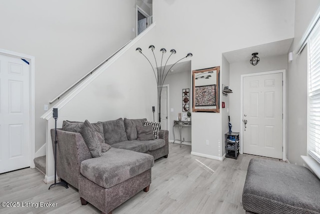 living room featuring stairway, baseboards, light wood-style floors, and a towering ceiling