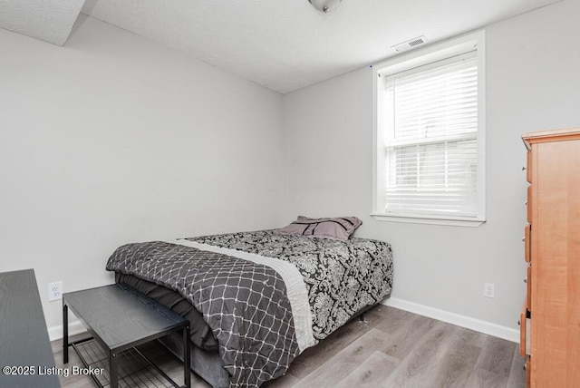 bedroom with visible vents, baseboards, and wood finished floors