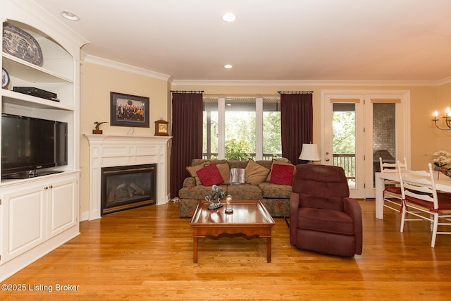 living room with a glass covered fireplace, light wood-style flooring, ornamental molding, and recessed lighting