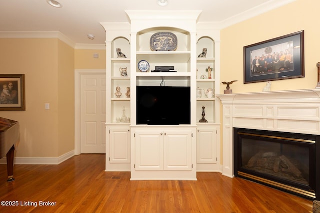 unfurnished living room with crown molding, baseboards, built in features, light wood-style flooring, and a glass covered fireplace