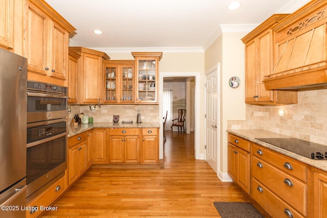 kitchen featuring custom range hood, freestanding refrigerator, light wood-style floors, black electric cooktop, and light stone countertops