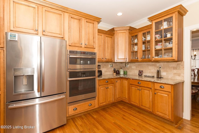 kitchen featuring decorative backsplash, light stone countertops, light wood-style floors, and appliances with stainless steel finishes