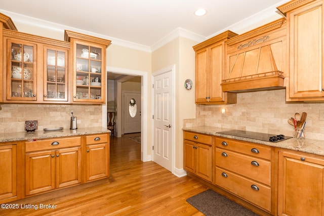 kitchen with crown molding, glass insert cabinets, black electric stovetop, light wood-style floors, and custom exhaust hood