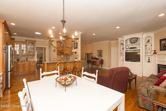 dining area featuring a glass covered fireplace, recessed lighting, wood finished floors, and ornamental molding