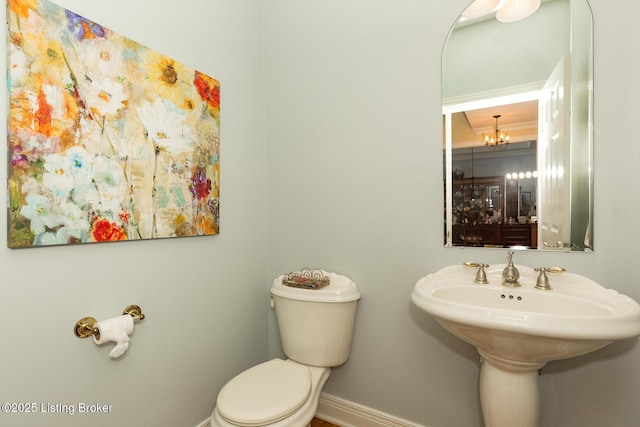 half bathroom featuring a notable chandelier, toilet, and baseboards