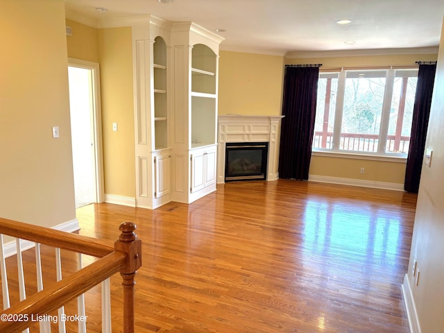 unfurnished living room featuring a glass covered fireplace, ornamental molding, baseboards, and wood finished floors