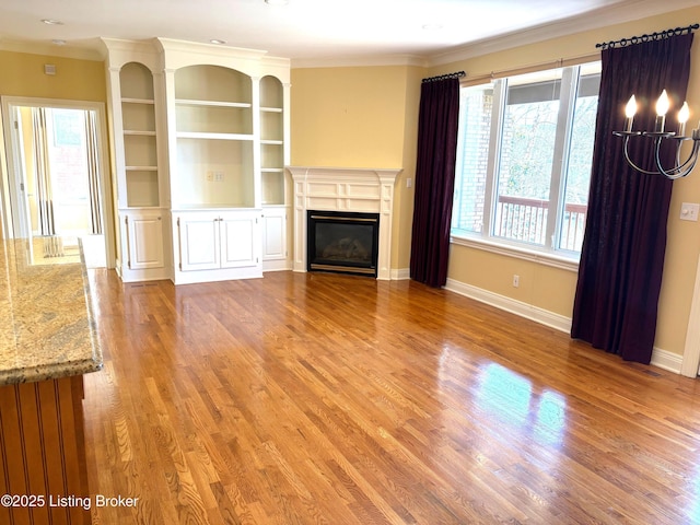 unfurnished living room featuring built in shelves, baseboards, ornamental molding, light wood-style floors, and a glass covered fireplace