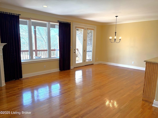 spare room with ornamental molding, a fireplace, light wood finished floors, baseboards, and a chandelier