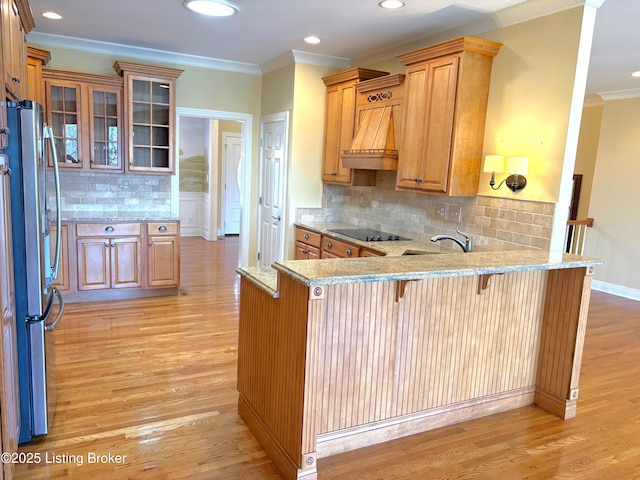 kitchen with a peninsula, freestanding refrigerator, light wood-style floors, a kitchen bar, and black electric cooktop