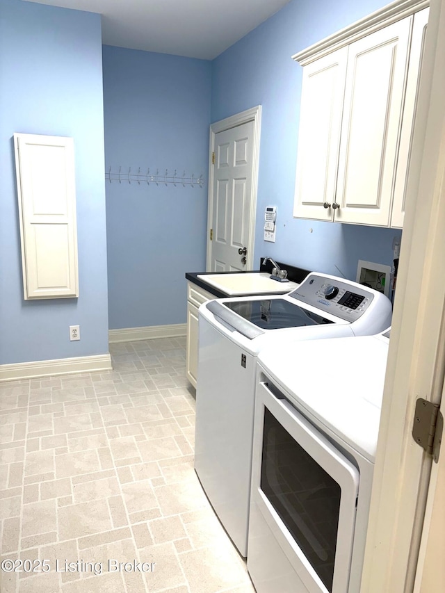 washroom with a sink, baseboards, brick floor, cabinet space, and separate washer and dryer