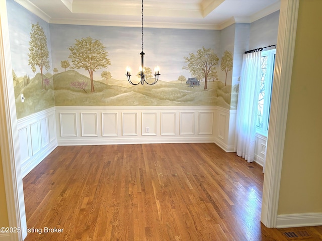 unfurnished dining area featuring a raised ceiling, a notable chandelier, wood finished floors, and visible vents