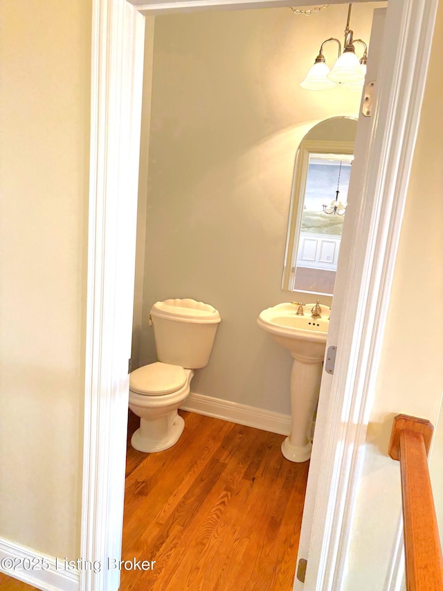 bathroom with a notable chandelier, toilet, wood finished floors, and baseboards