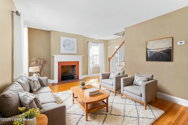 living area with light wood finished floors, stairway, a brick fireplace, and baseboards