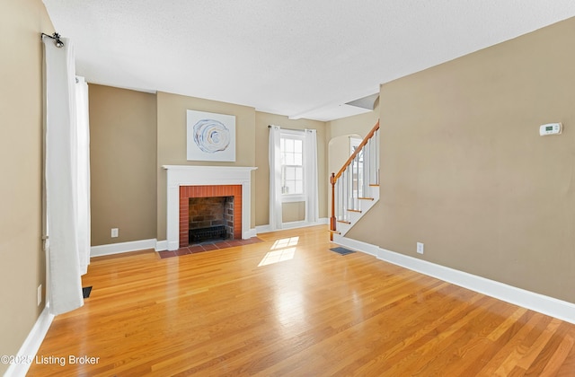 unfurnished living room with baseboards, a fireplace, stairway, and light wood finished floors