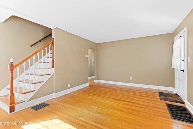 unfurnished living room with arched walkways, visible vents, baseboards, and wood finished floors