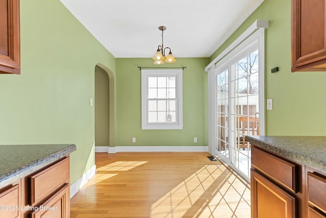 dining space featuring arched walkways, light wood-type flooring, a chandelier, and baseboards