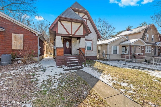 tudor-style house featuring central AC unit, fence, and stucco siding