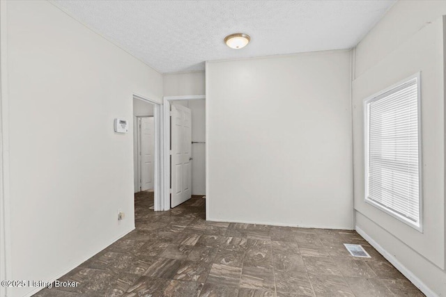 unfurnished room featuring a textured ceiling, dark floors, and visible vents