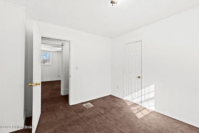 unfurnished bedroom with a textured ceiling, dark colored carpet, and visible vents