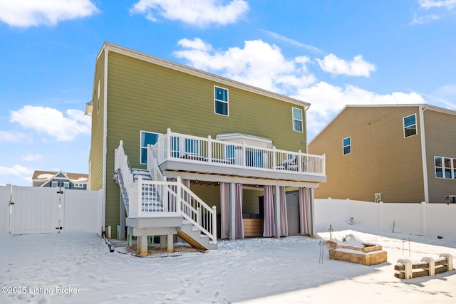 snow covered rear of property featuring stairs, a deck, fence, and a gate