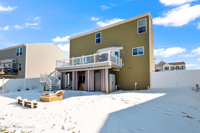 snow covered house with fence, stairway, and a wooden deck