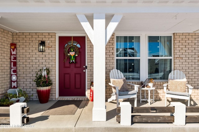 view of exterior entry featuring covered porch and brick siding