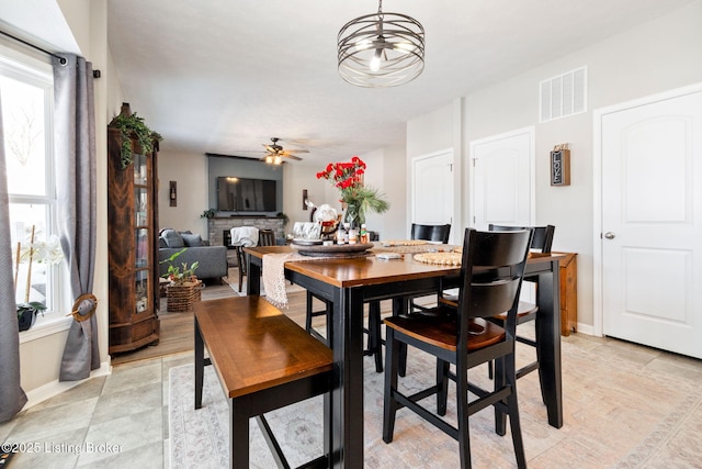 dining space with ceiling fan, a wealth of natural light, a fireplace, and visible vents