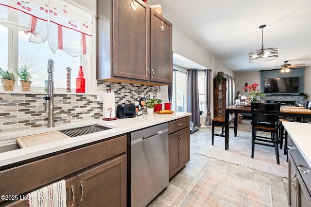 kitchen featuring decorative backsplash, hanging light fixtures, light countertops, stainless steel dishwasher, and a sink