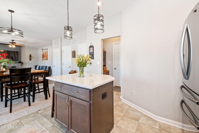 kitchen featuring a center island, decorative light fixtures, a ceiling fan, freestanding refrigerator, and dark brown cabinets