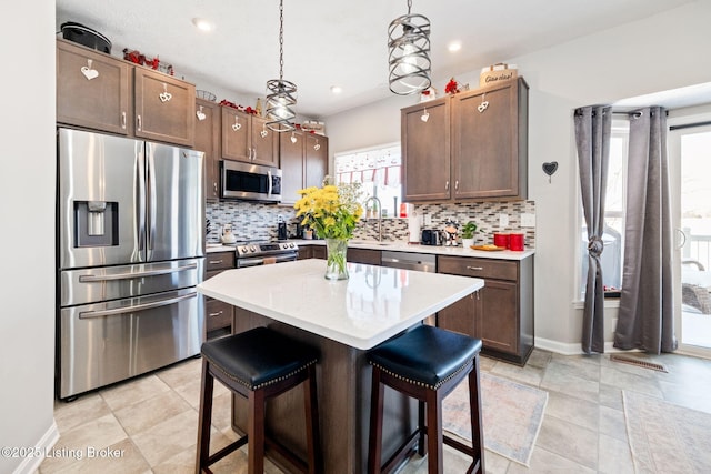 kitchen with a kitchen island, appliances with stainless steel finishes, a breakfast bar area, hanging light fixtures, and light countertops