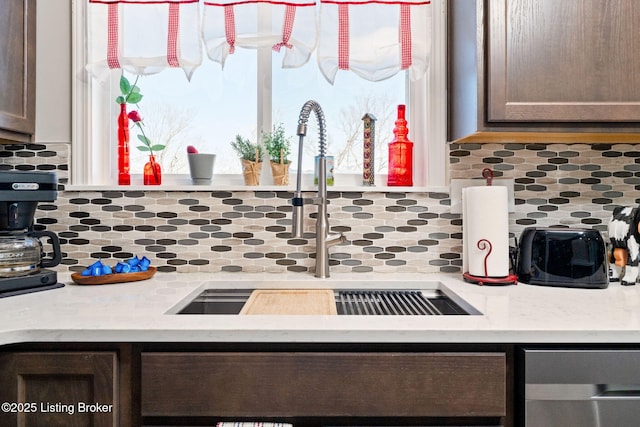 kitchen featuring light countertops, dark brown cabinets, backsplash, and a sink