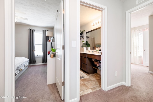 corridor with a textured ceiling, baseboards, and light colored carpet