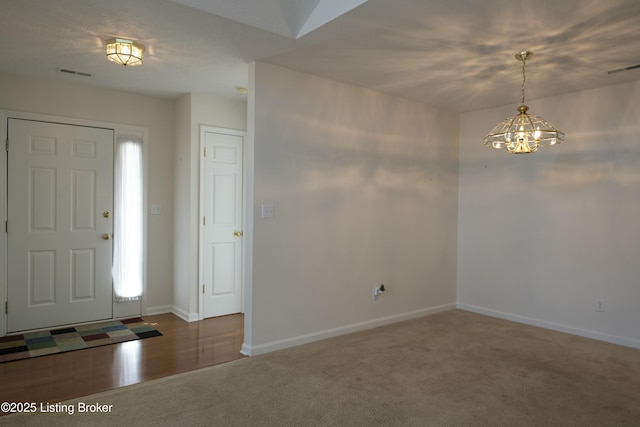 carpeted entrance foyer featuring visible vents, baseboards, and an inviting chandelier