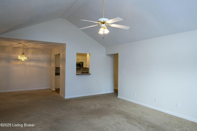 unfurnished living room with ceiling fan with notable chandelier, high vaulted ceiling, carpet flooring, and baseboards