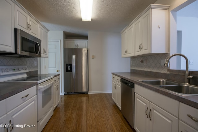 kitchen with white cabinets, dark countertops, appliances with stainless steel finishes, dark wood-style flooring, and a sink