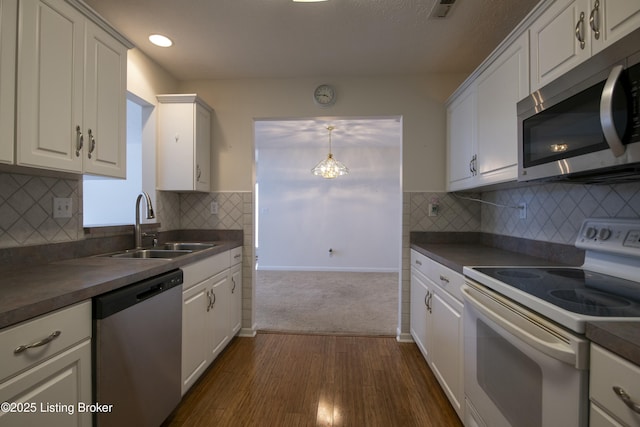 kitchen with appliances with stainless steel finishes, dark countertops, a sink, and white cabinetry