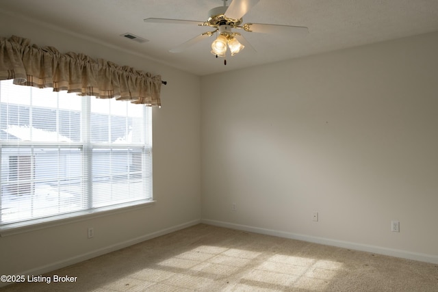 empty room featuring light carpet, ceiling fan, visible vents, and baseboards