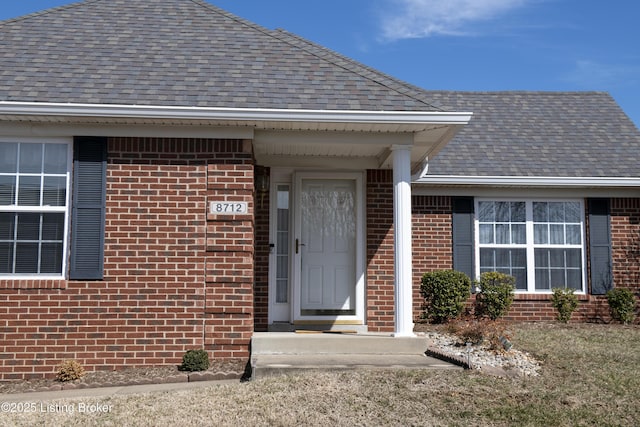 entrance to property featuring a shingled roof and brick siding