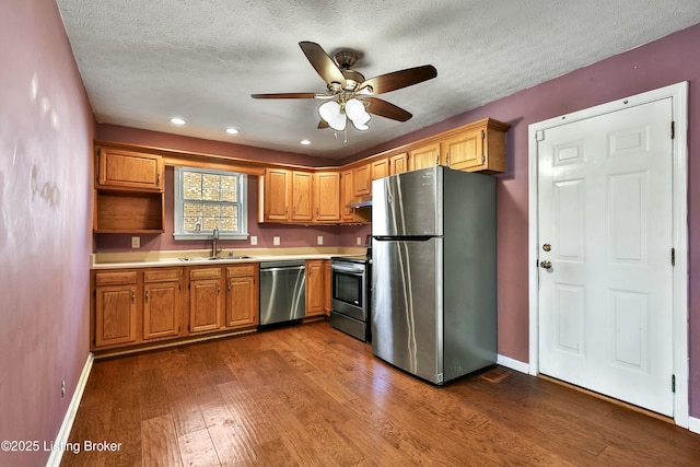 kitchen featuring dark wood-style floors, stainless steel appliances, light countertops, a sink, and baseboards