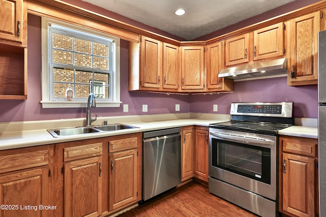 kitchen featuring under cabinet range hood, dark wood-style flooring, a sink, light countertops, and appliances with stainless steel finishes