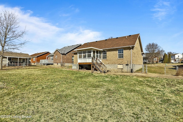 rear view of property featuring a sunroom, fence, a lawn, and brick siding