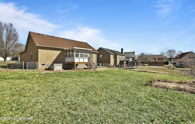 rear view of property featuring a sunroom, brick siding, a lawn, and a fenced backyard