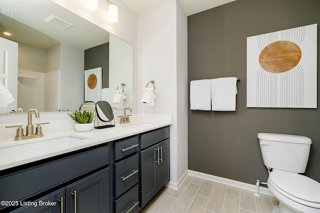 bathroom with double vanity, a sink, toilet, and baseboards