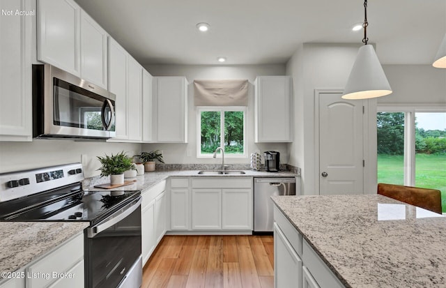 kitchen with light stone counters, stainless steel appliances, a sink, white cabinets, and light wood-type flooring