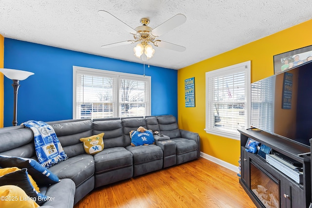 living room featuring ceiling fan, a textured ceiling, light wood-style flooring, and baseboards