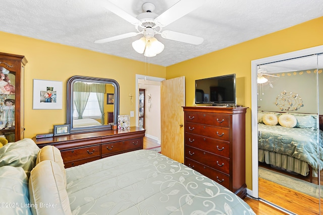 bedroom with light wood-style flooring, a textured ceiling, baseboards, and a ceiling fan